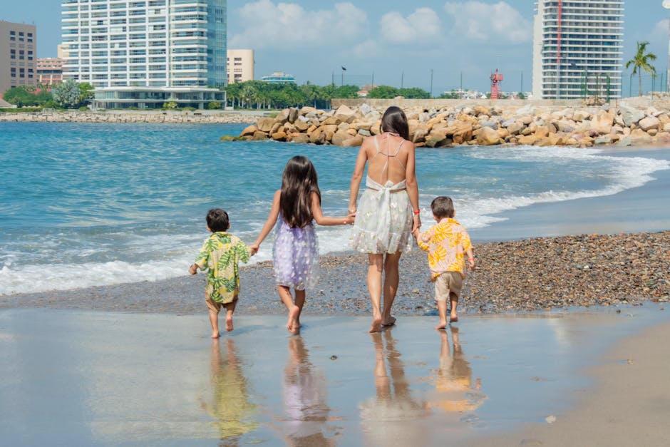 A family enjoys a sunny beach day with children playing in the sand and waves.