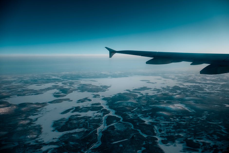 Aircraft flying high in air against blue sky with skyline above frozen terrain covered with snow in nature on winter day