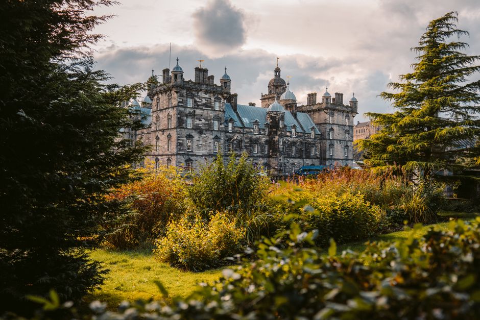 A picturesque view of an ancient castle surrounded by vibrant greenery under a cloudy sky.