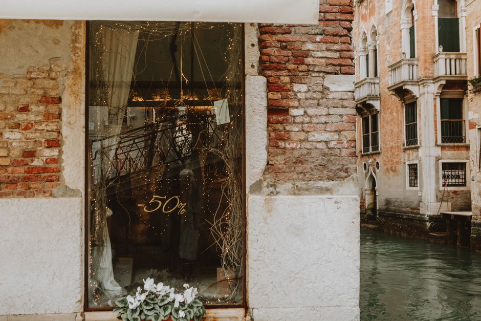 A charming Venetian storefront with a 50% sale sign and festive string lights.