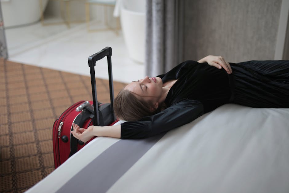 A woman resting on a hotel bed beside her suitcase, capturing travel fatigue.