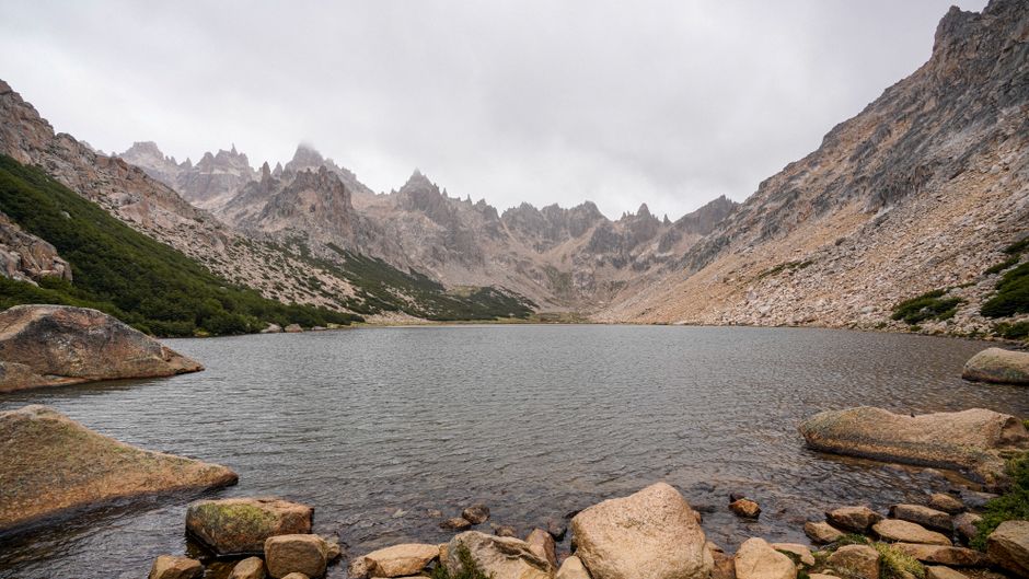 A breathtaking view of a serene mountain lake surrounded by dramatic rocky peaks under cloudy skies.