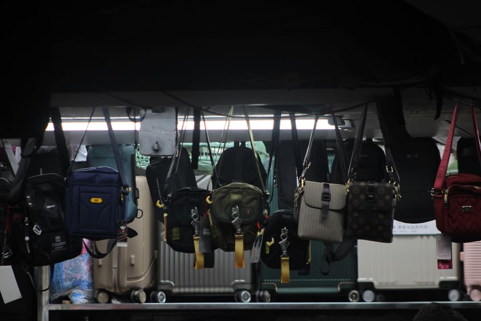 Colorful bags and luggage hang on display in a dimly lit market setting.