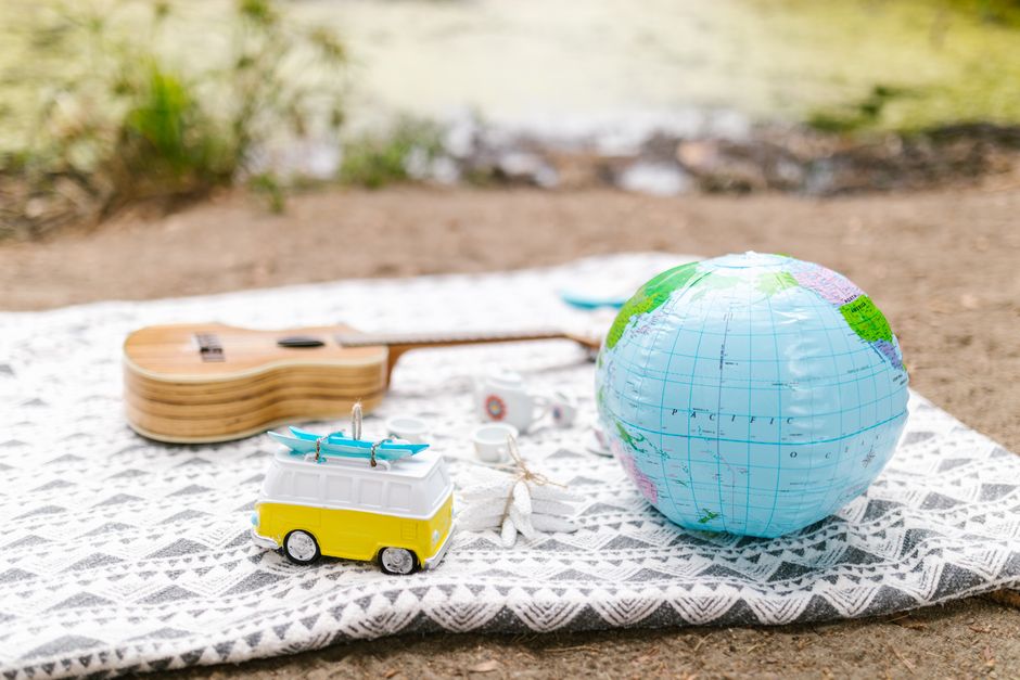 A cosy outdoor picnic setup featuring a globe, toy van, and guitar on a blanket by the water.