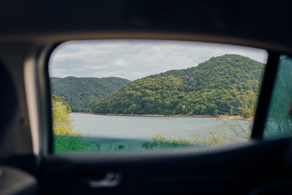 View of lush green hills and serene lake from the backseat of a car.