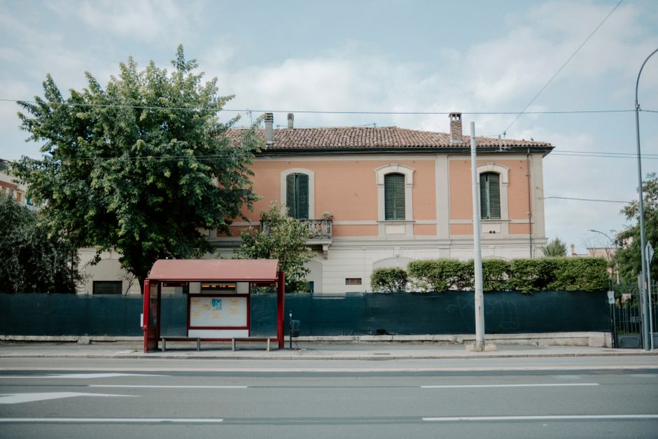 A suburban bus stop in front of a historic building on a quiet street, showcasing urban transit.