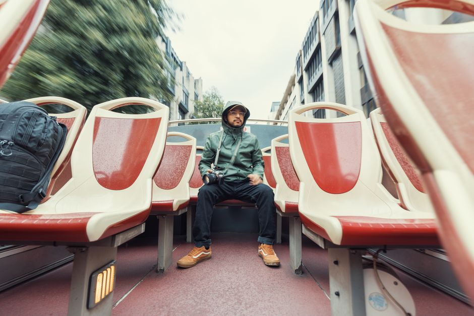A man in a raincoat sits alone on an open-top tour bus, capturing urban scenes.