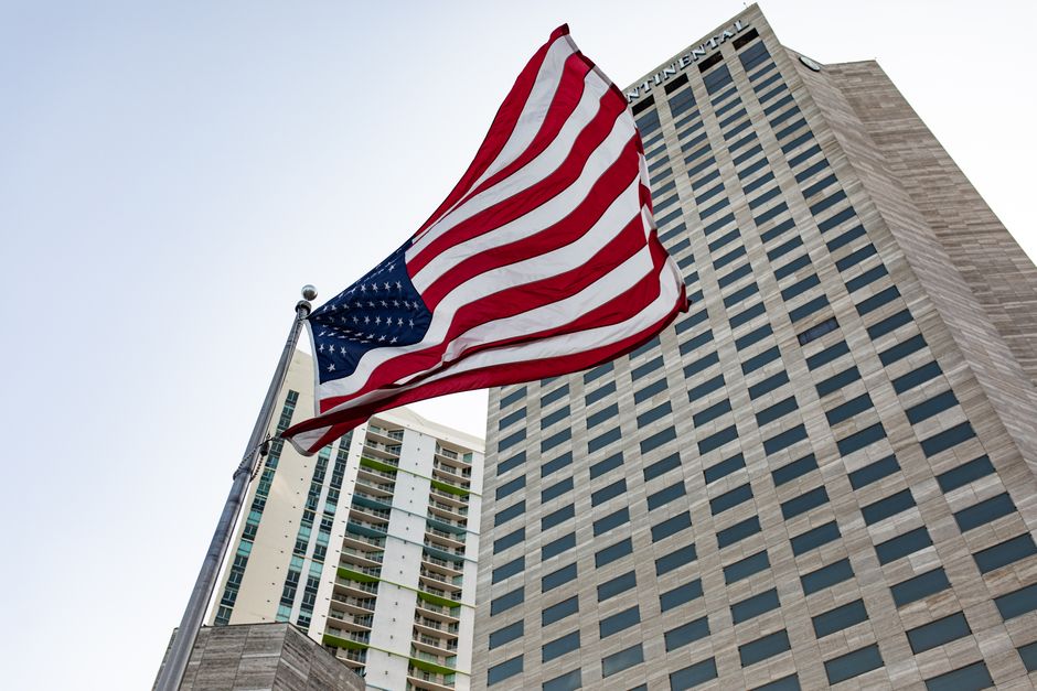 Low angle view of American flag and modern skyscraper in USA cityscape.