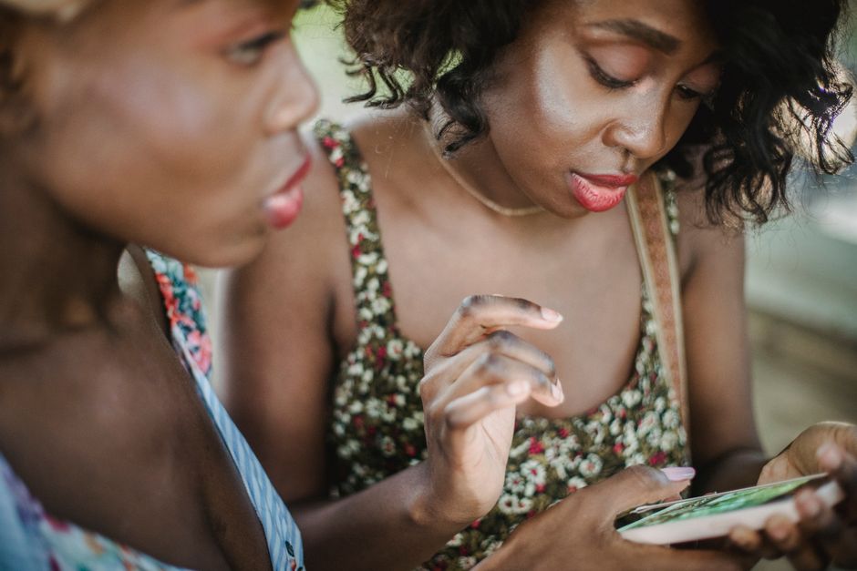 Two women in floral dresses enjoying a moment together using a smartphone.
