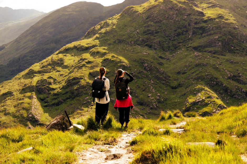 Two hikers enjoy a scenic trek in Killarney, Ireland, surrounded by lush green mountains.