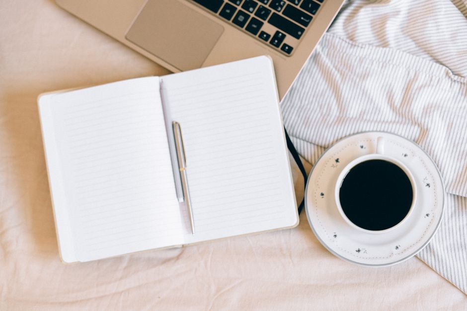 Cosy workspace setup with a laptop, notebook, and coffee cup on a soft blanket.