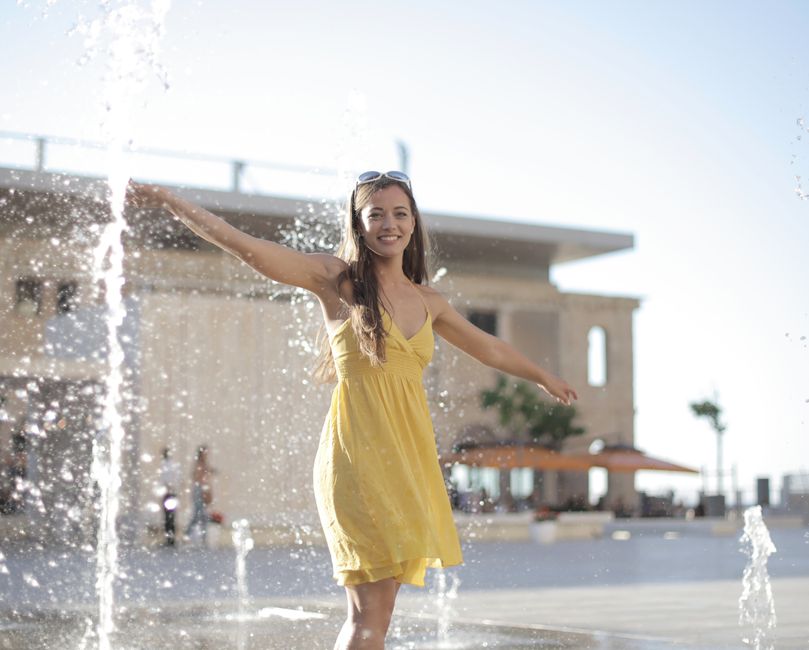 Joyful woman in a yellow dress enjoying a fun moment in a water fountain outdoors.