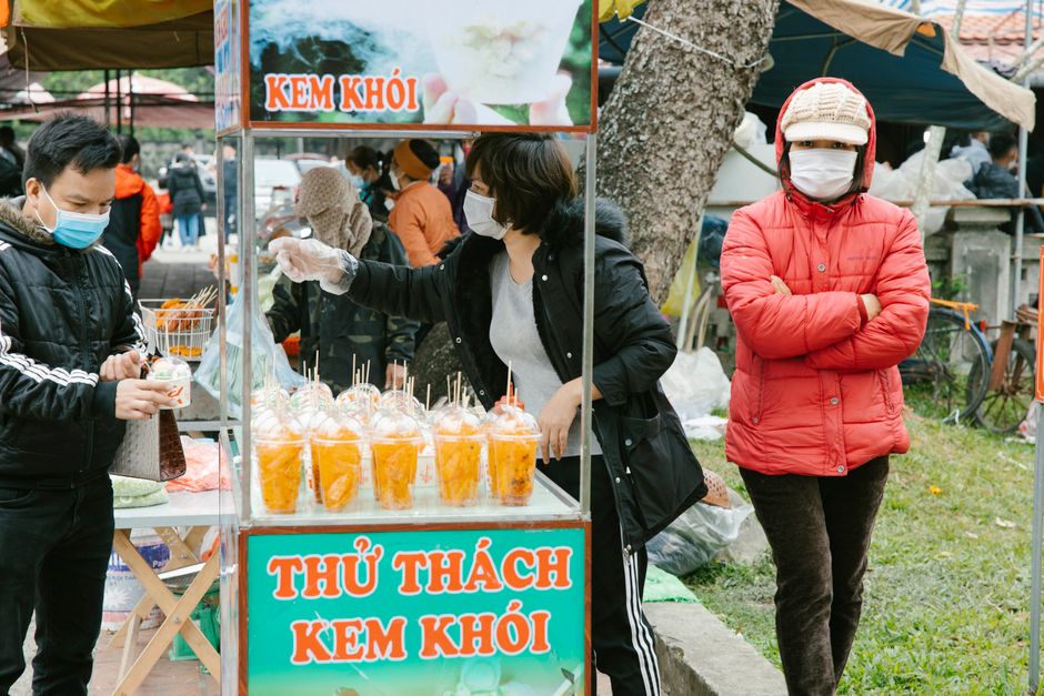 People buying snacks at an outdoor food stand in Hà Nam, Vietnam street market.