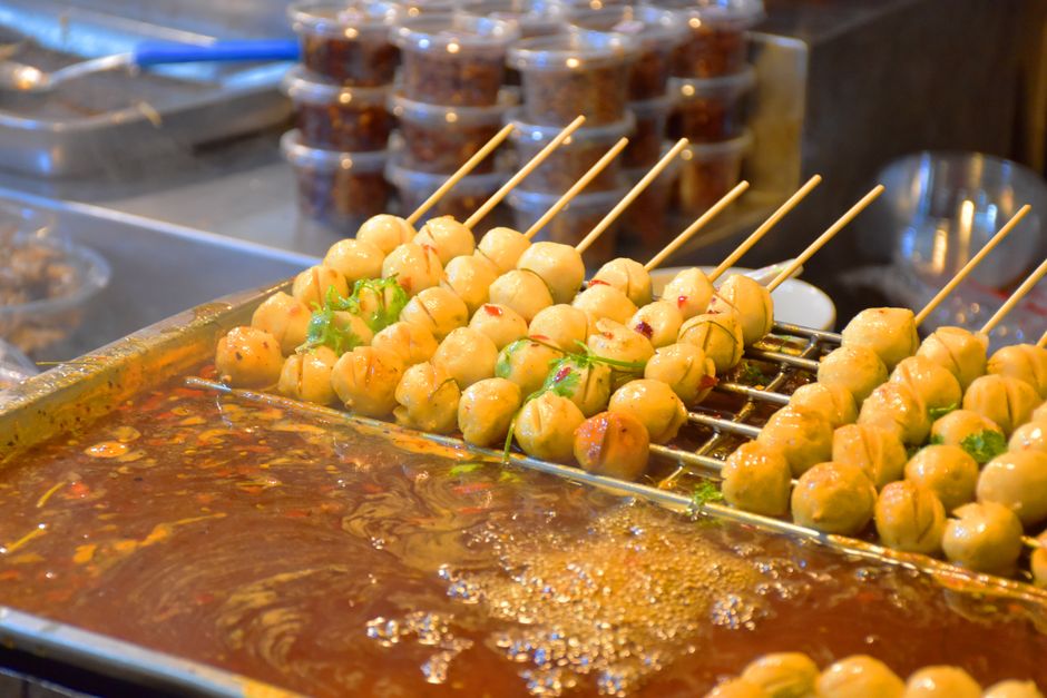 Close-up of skewered meatballs cooking in spicy sauce at street food stall.