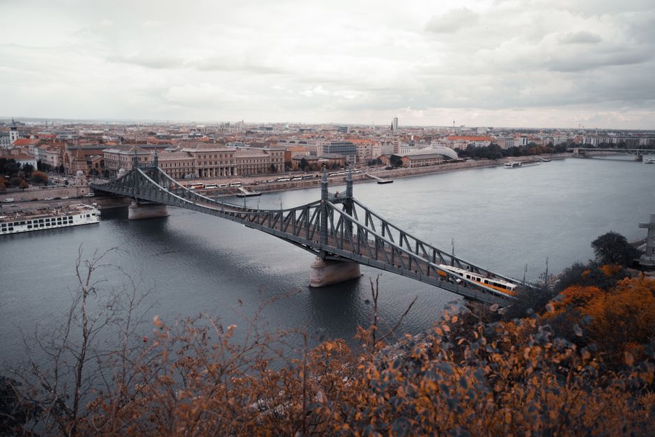 A scenic view of Liberty Bridge spanning the Danube River in autumn with Budapest cityscape backdrop.