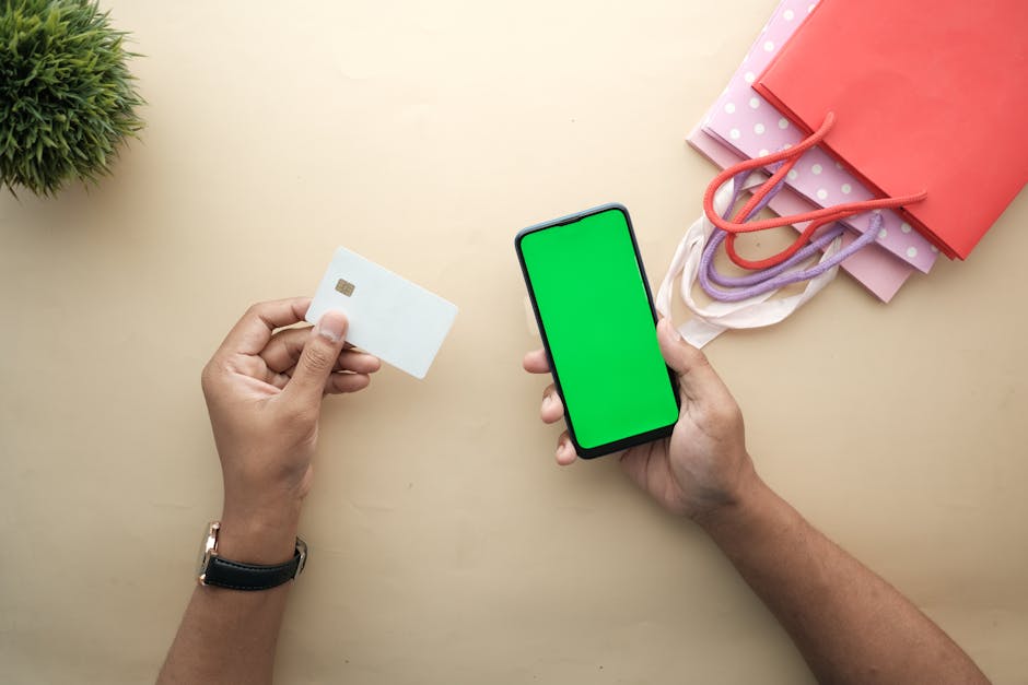 Top view of hands holding a smartphone and credit card for online shopping on a beige background.