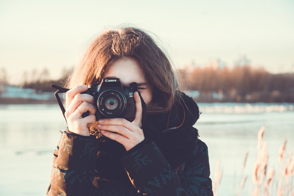 A woman using a camera captures a winter landscape outdoors, wearing a warm jacket.