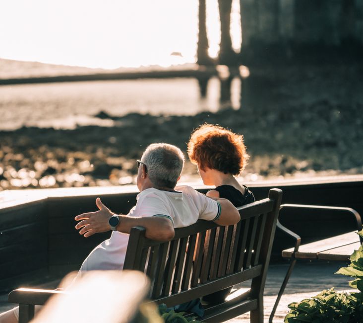 Older couple sitting on a bench enjoying a seaside sunset in Perillo, GA, Spain.
