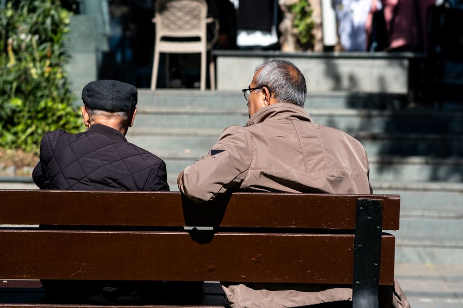 Two senior men enjoying a sunny day on a park bench, engaged in conversation.