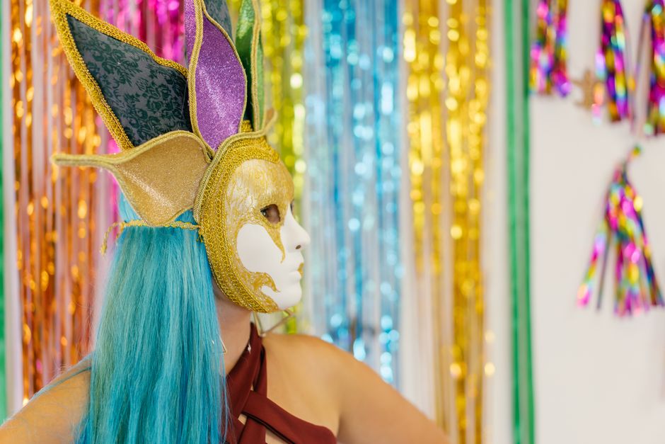 A vibrant masquerade scene with a person in an elaborate mask and festive backdrop.