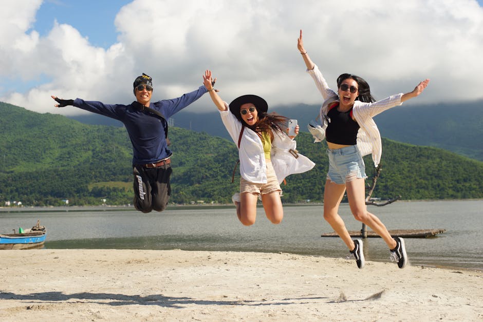 A joyful moment captured as three friends jump on a beach with lush green mountains in the background.