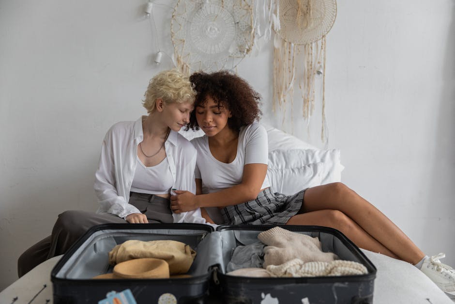Multiracial young girlfriends in casual clothes embracing with closed eyes while packing suitcase in cozy bedroom